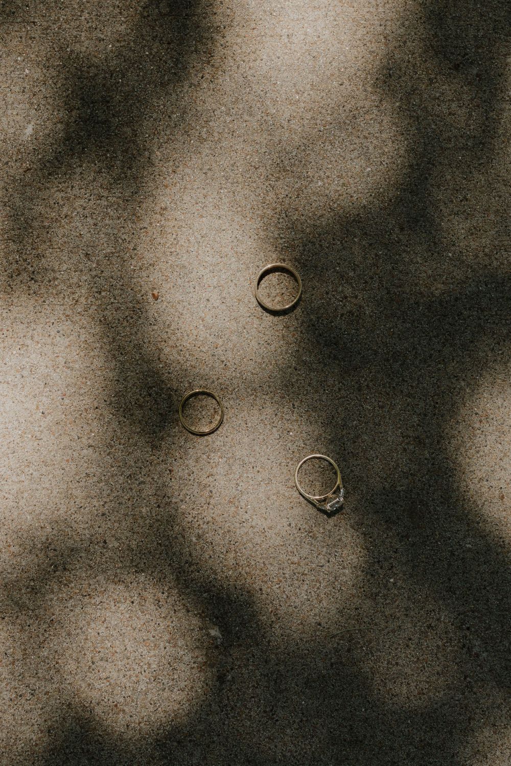 Wedding rings casting dramatic shadows on textured beige surface.