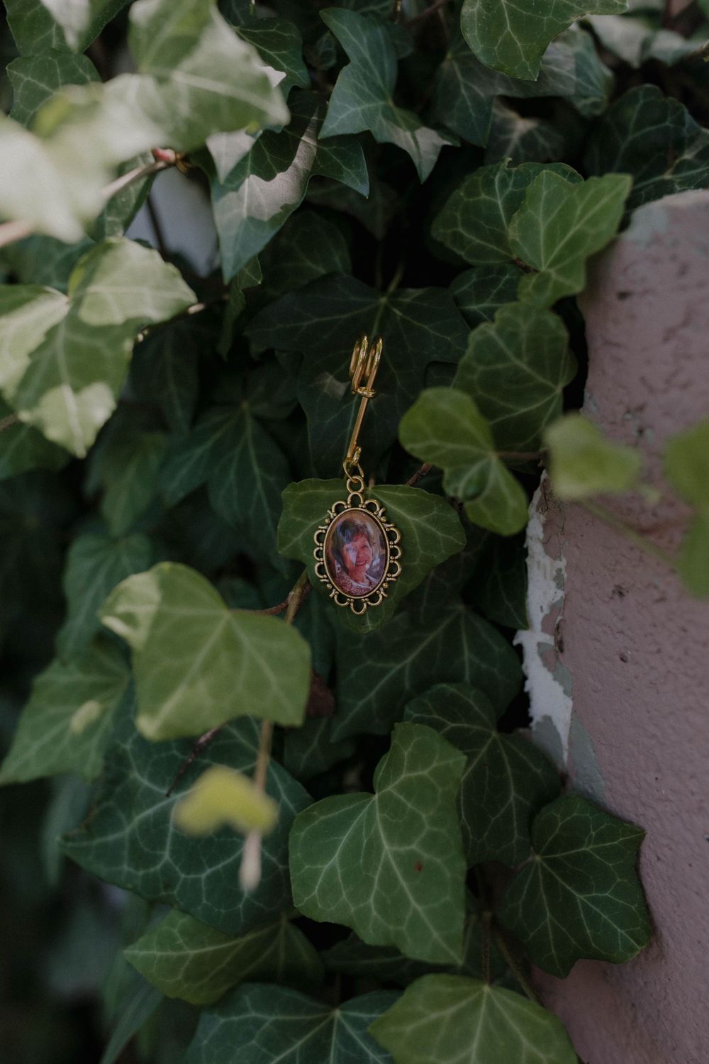 Delicate jewelry pieces hanging among green ivy leaves on a stone wall.