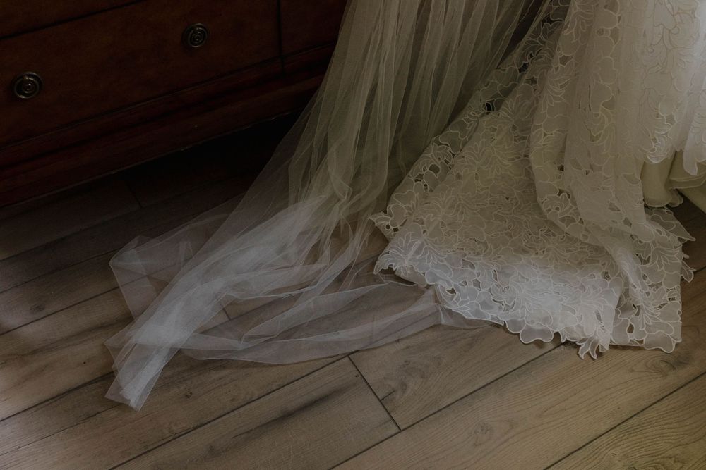Flowing white wedding dress with lace details and long train displayed on a dark hardwood floor.