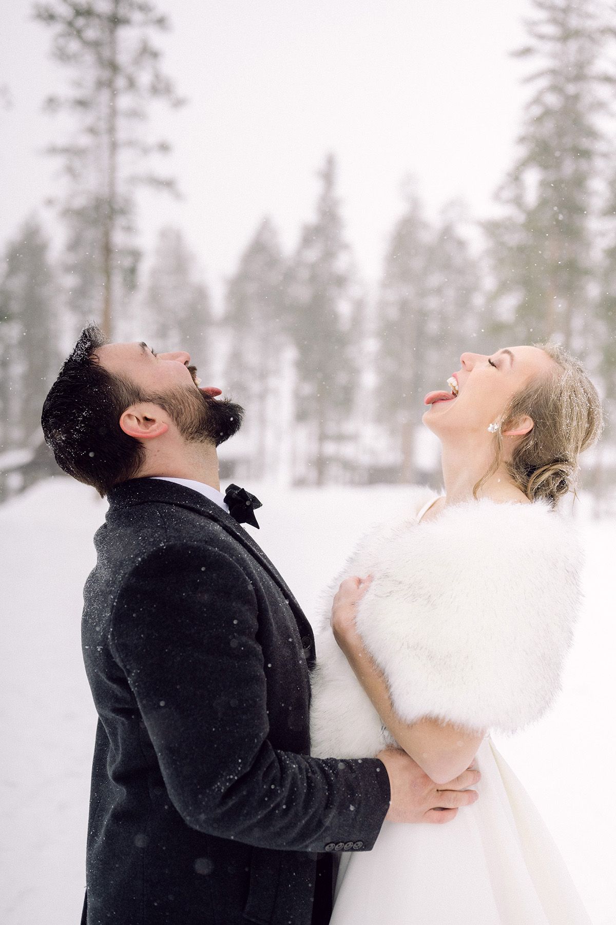 A joyful winter wedding moment with the newlyweds laughing in the snow.