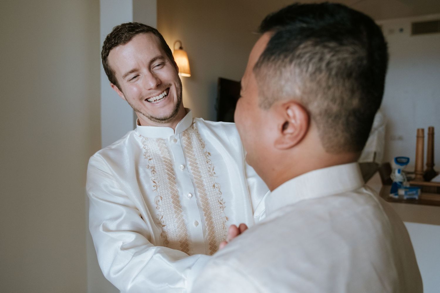 Two people in white traditional embroidered shirts sharing a joyful moment indoors.