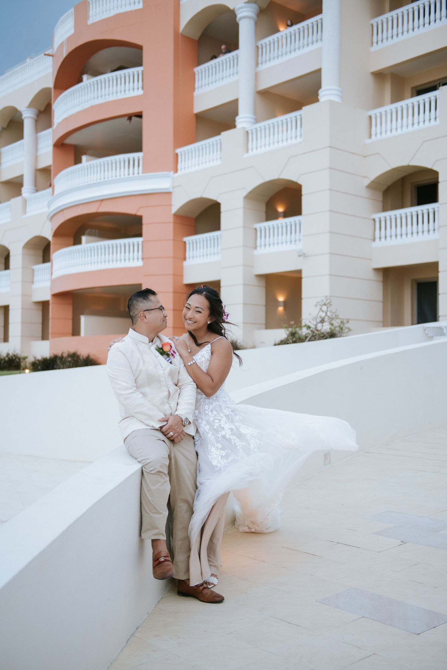 Couple sharing a romantic moment on white steps of a pink and white resort building.