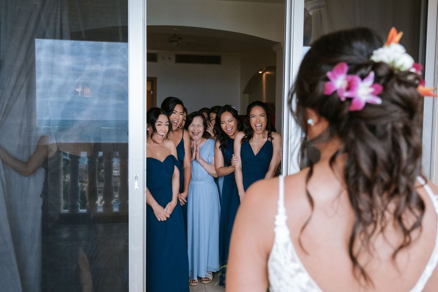 Wedding party in navy blue dresses reacting with excitement through glass door.