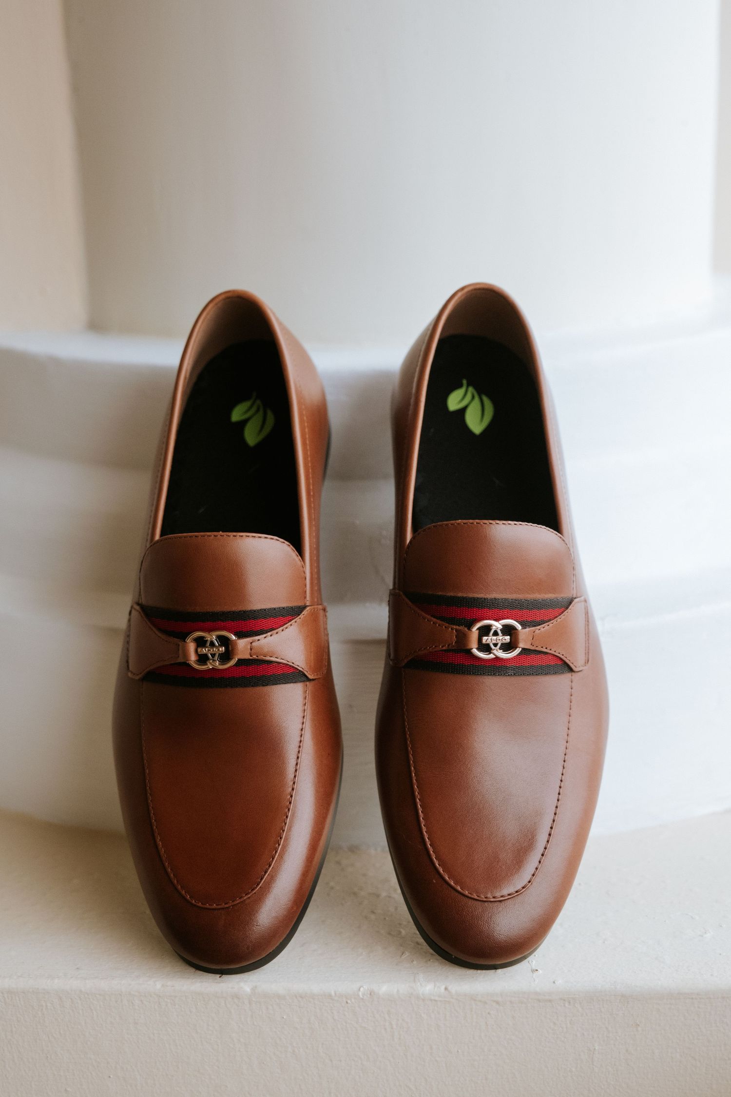 Brown leather loafers with decorative buckle detail displayed against white background.