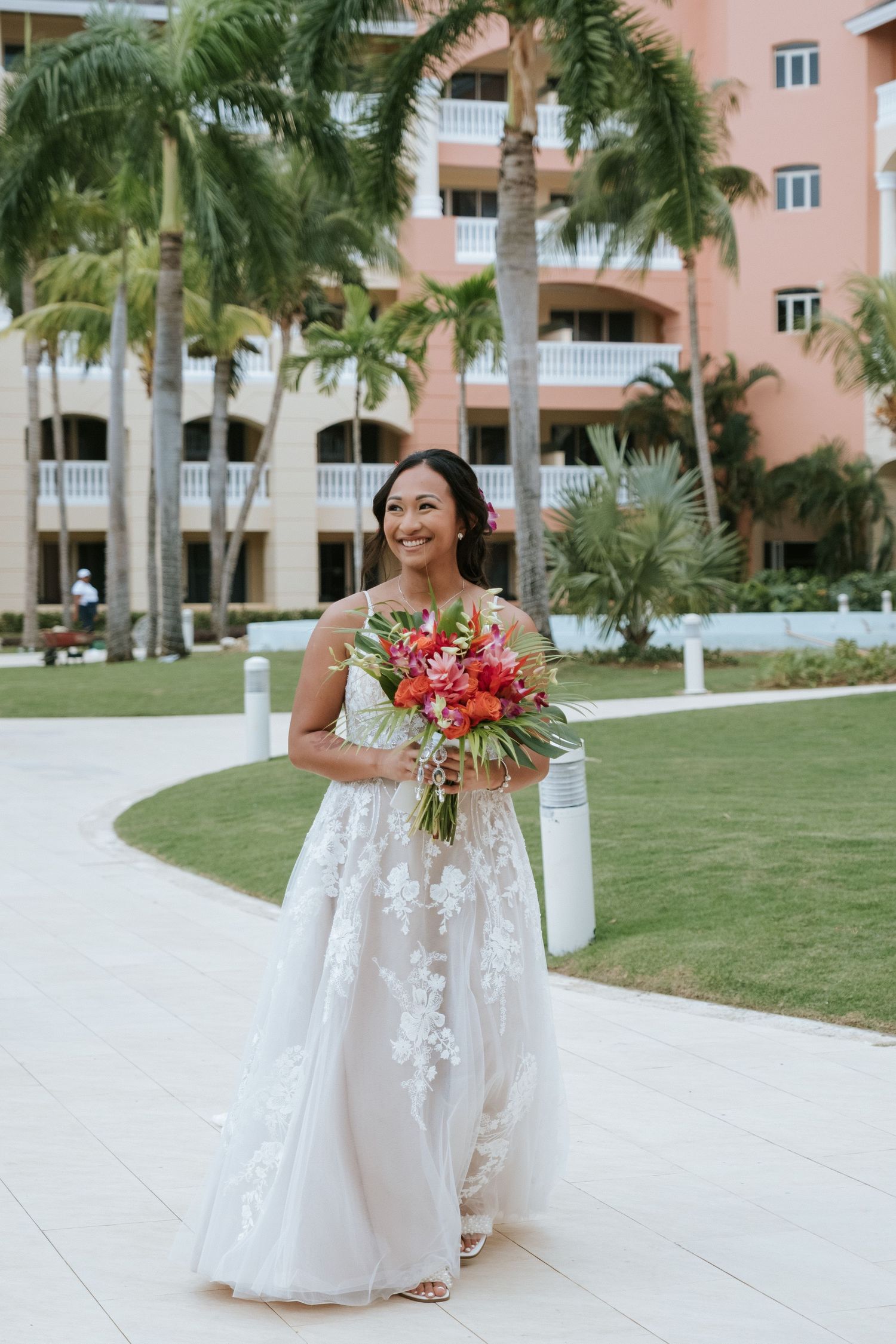 A bride walking outdoors holding a tropical bouquet at a beachside resort.
