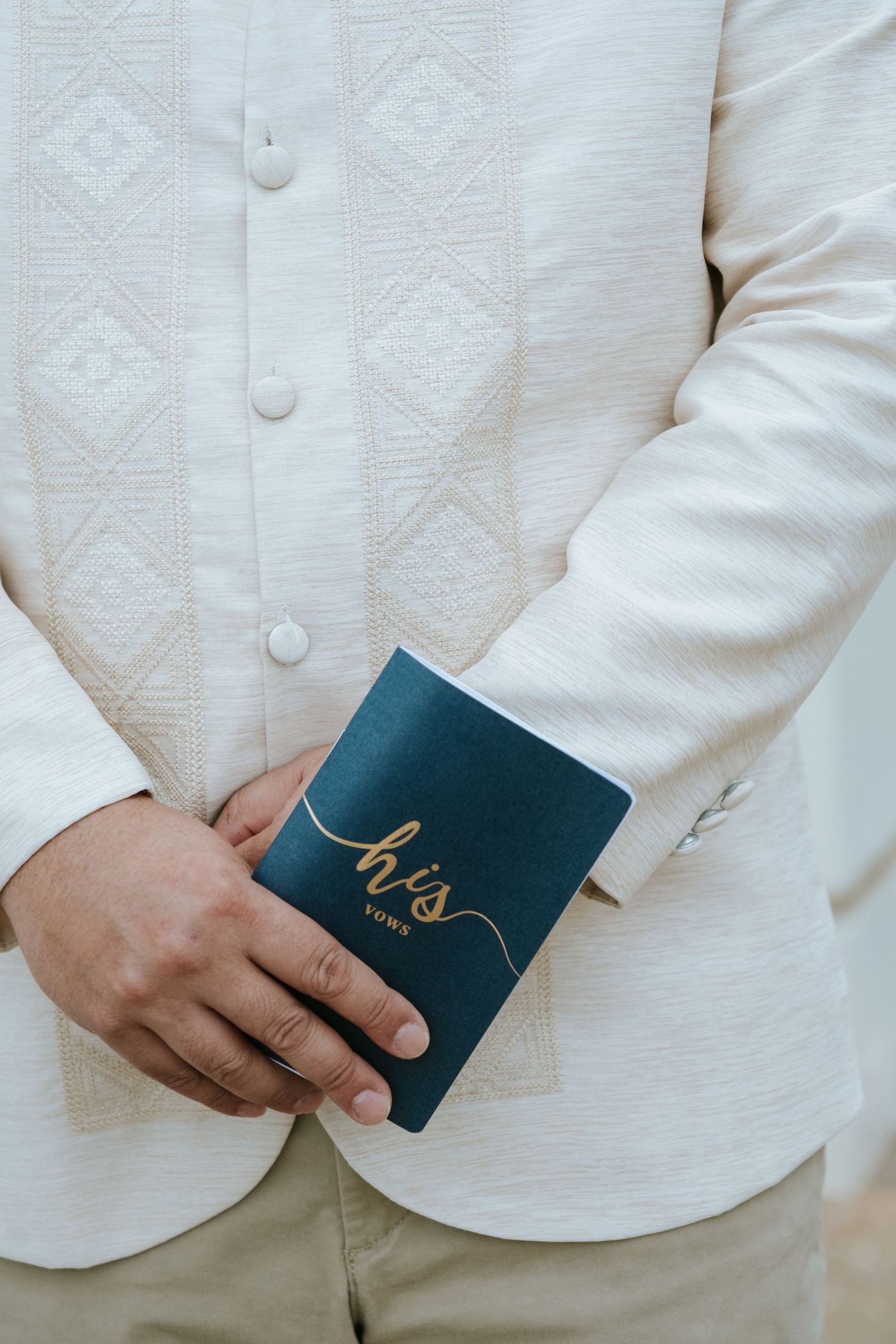 Hands holding a navy blue vows book with gold lettering against a white textured jacket.