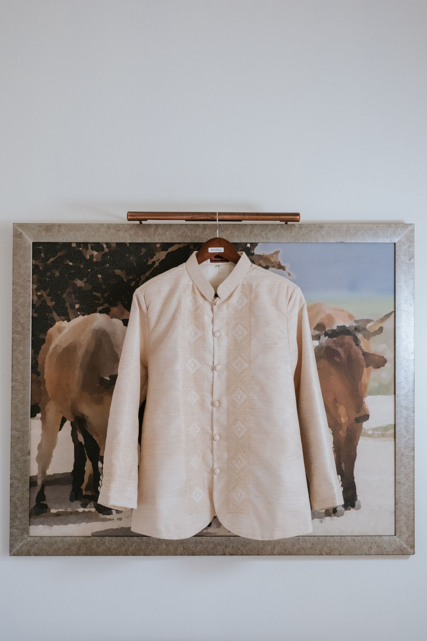 White formal jacket displayed in frame with cow photograph background.