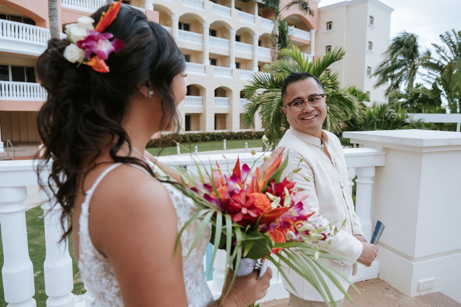 Two people in wedding attire sharing candid laughter on a balcony.