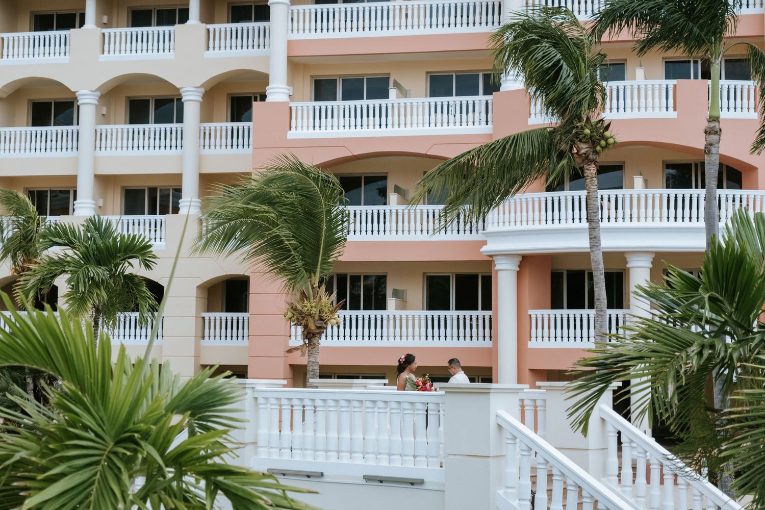 A pink resort building with white balconies and tropical landscaping in the foreground.