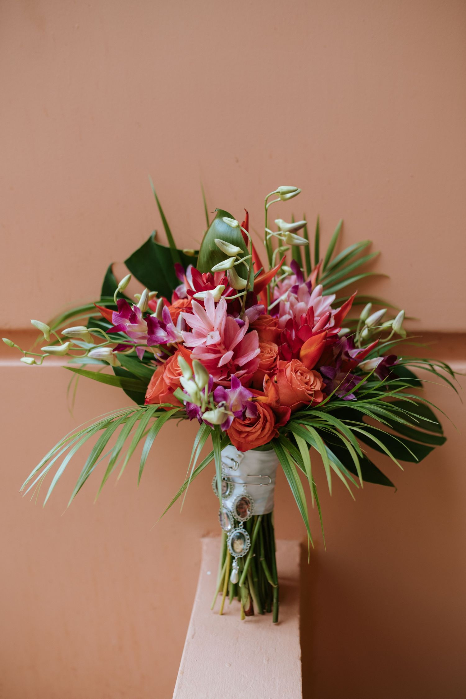 Vibrant tropical wedding bouquet with pink and red flowers wrapped in white ribbon.