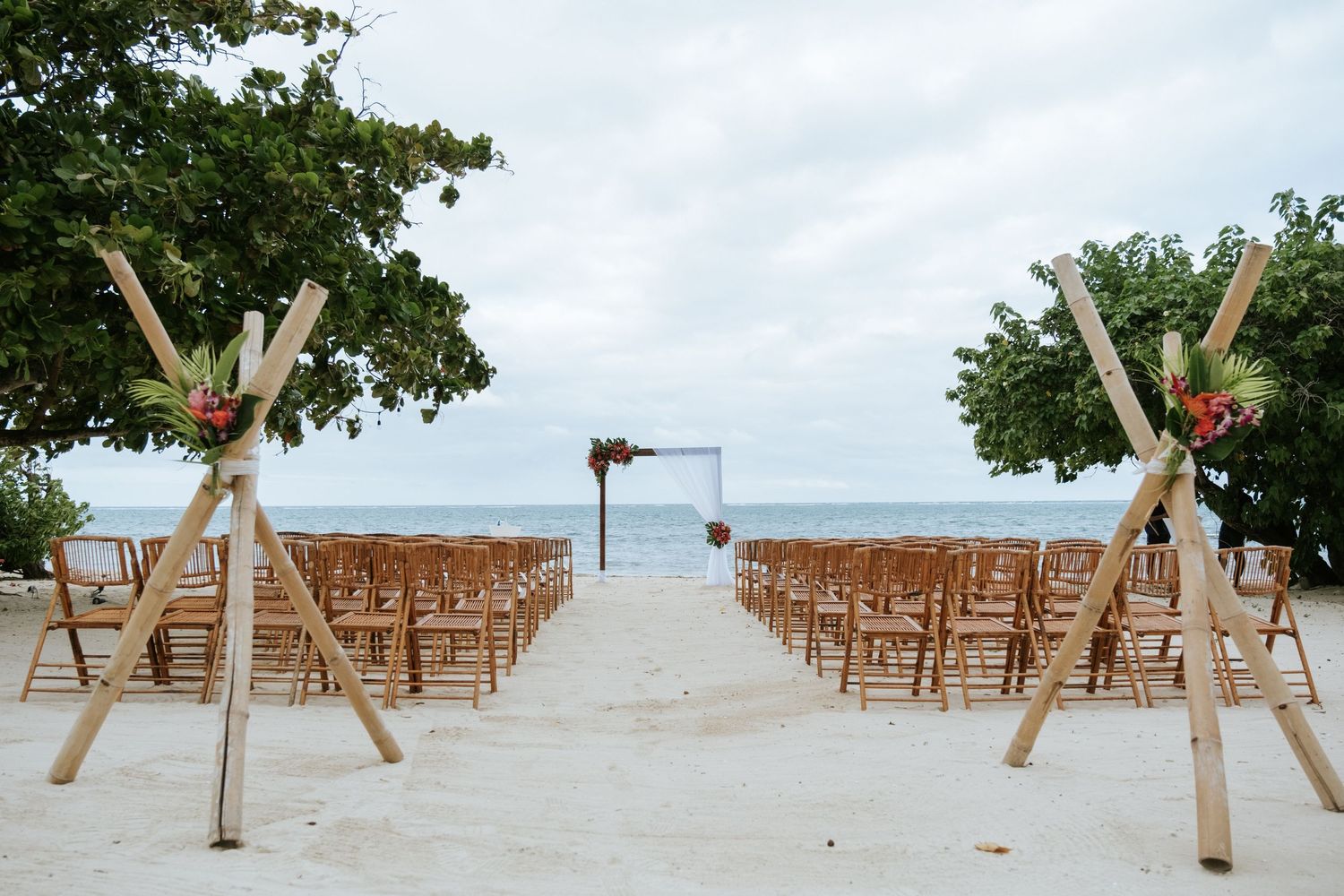 Beach wedding ceremony setup with wooden chairs and cross-shaped decorations leading to an ocean view altar.
