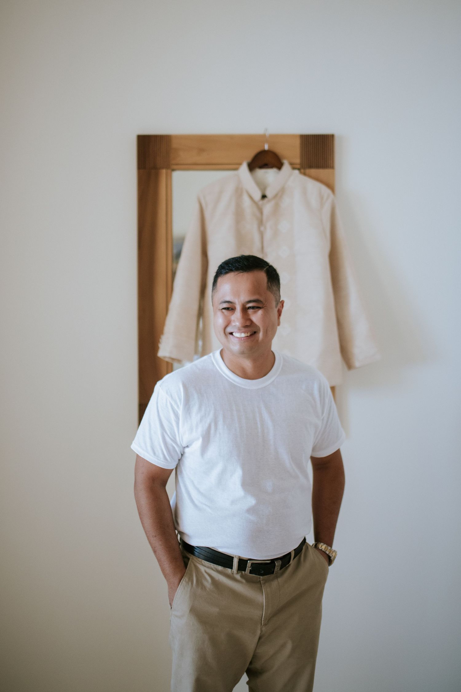 Person in white t-shirt and khakis standing against wall with cream jacket hanging above.