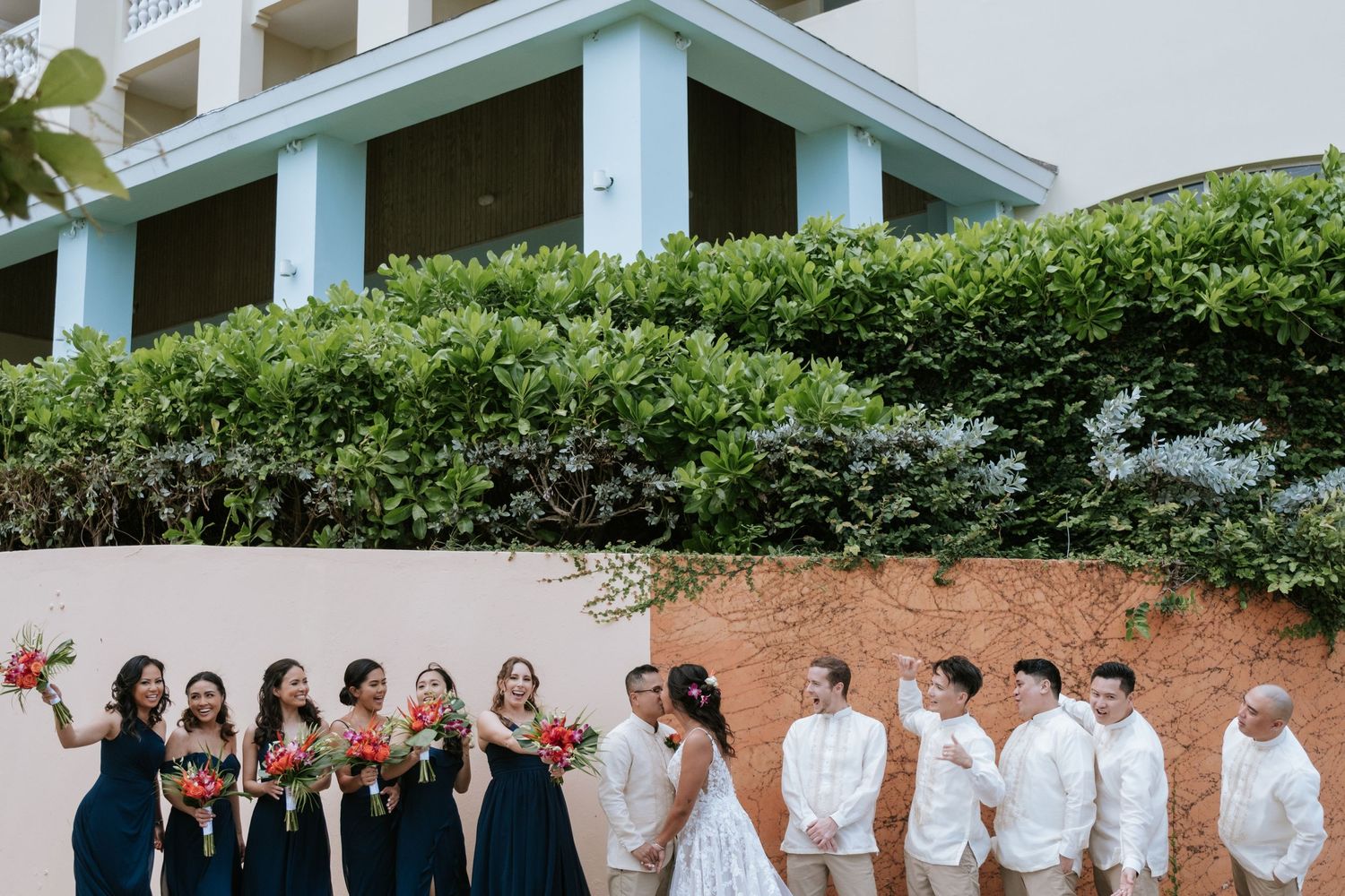 Wedding party in navy and white attire gathered outside a tropical resort building.