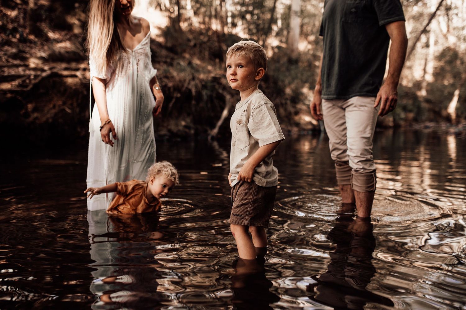 A family wades together in a peaceful forest stream during a sunny afternoon.