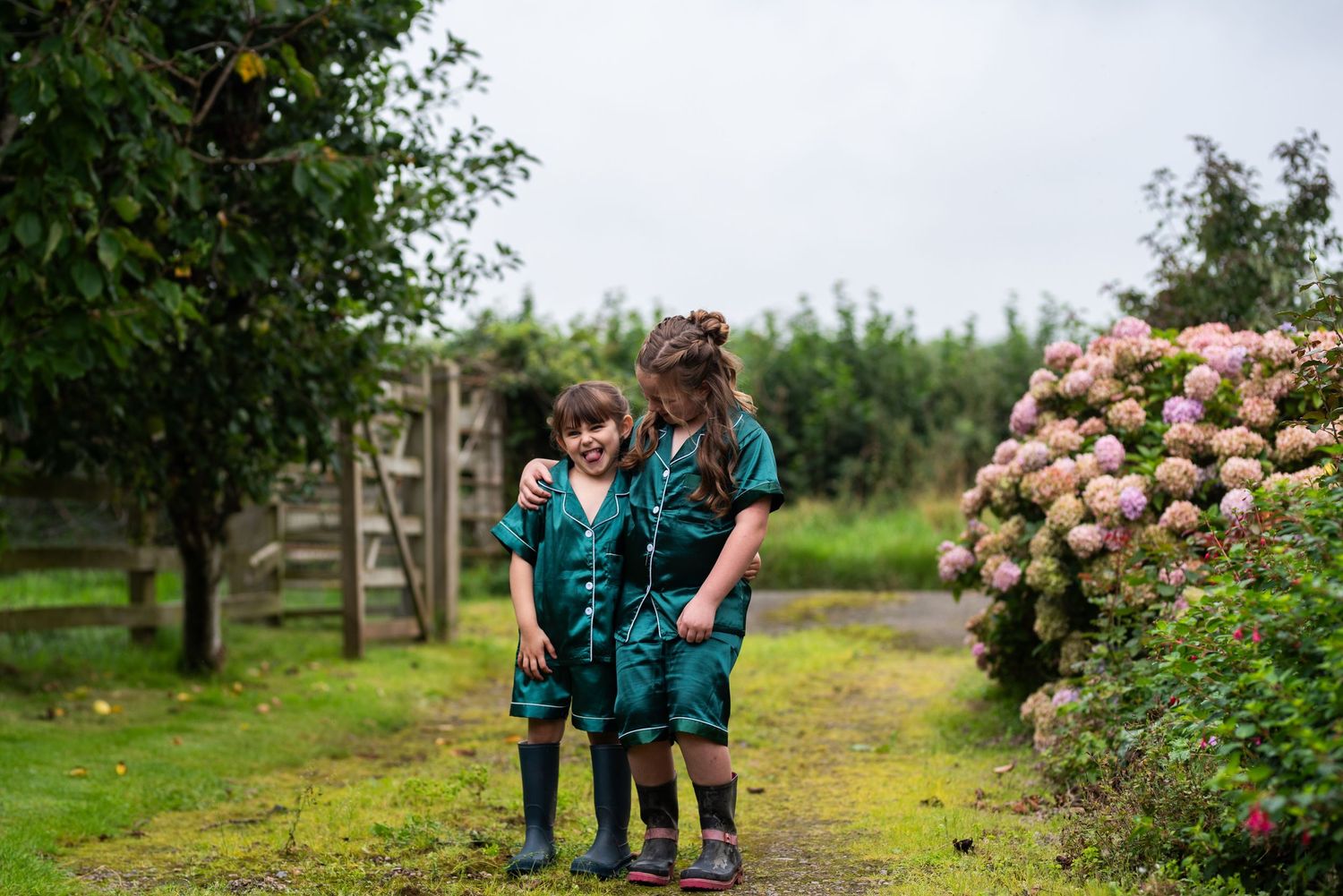 Two scouts in matching uniforms walking along garden path with blooming hydrangeas.