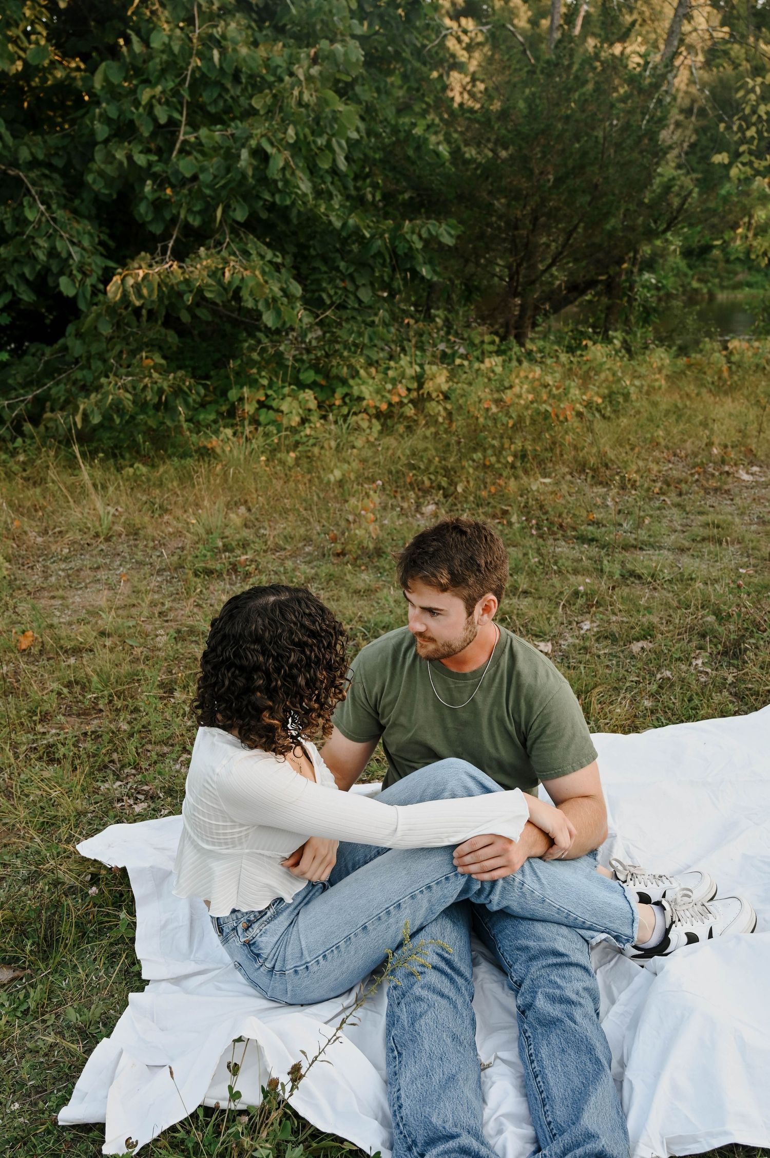 Couple sitting together on white blanket having intimate conversation in outdoor natural setting at sunset.