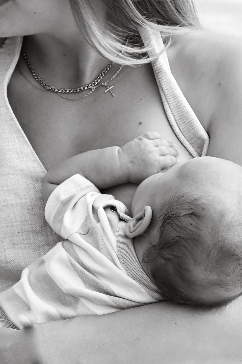 A tender black and white image shows a parent breastfeeding their baby, who wears a light-colored onesie.
