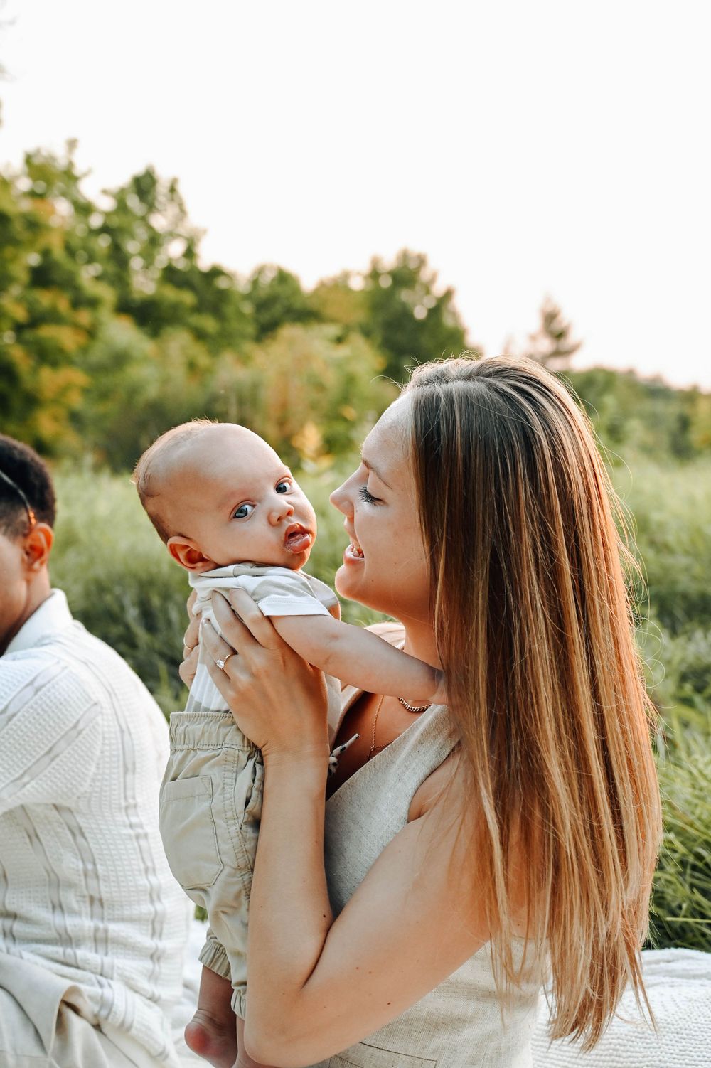 A tender moment between a parent and baby outdoors during a summer photoshoot with trees in the background.