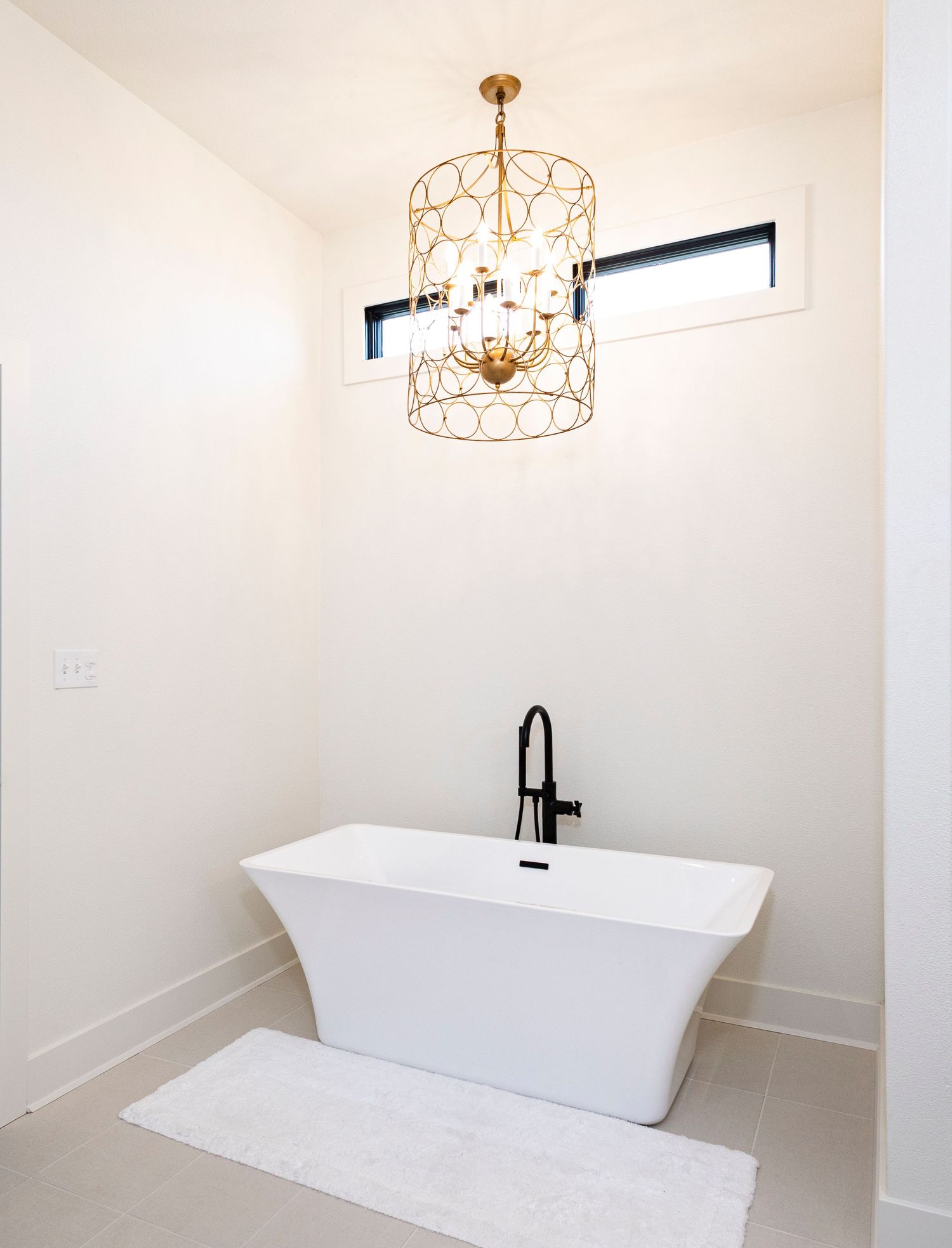 Modern white bathroom interior with freestanding bathtub and elegant copper chandelier lighting fixture.