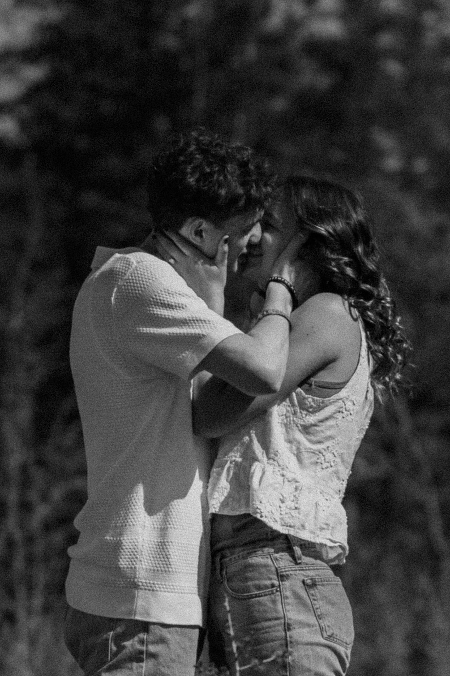 Black and white photo of a romantic couple almost kissing outdoors, woman touching man's face tenderly.