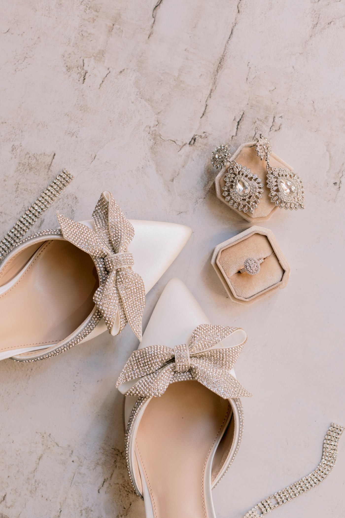 Elegant bridal accessories flat lay featuring crystal bow heels, diamond earrings, and engagement ring.