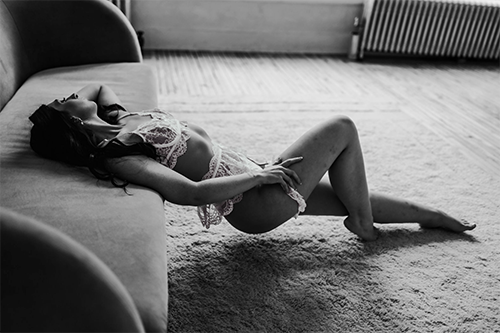 Black and white boudoir photo of a woman in lingerie reclining gracefully on a couch.