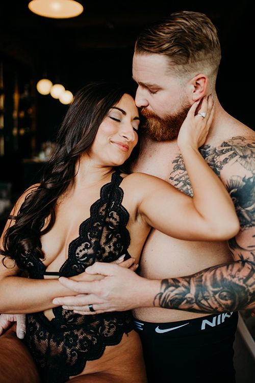 Romantic couple embracing tenderly, man with tattoos and woman in black lace lingerie.