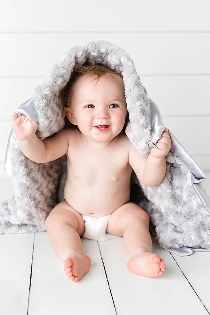 Wildomar baby photographer studio portrait of baby boy in diaper sitting on white wood floor holding up a soft Minky Couture blanket.