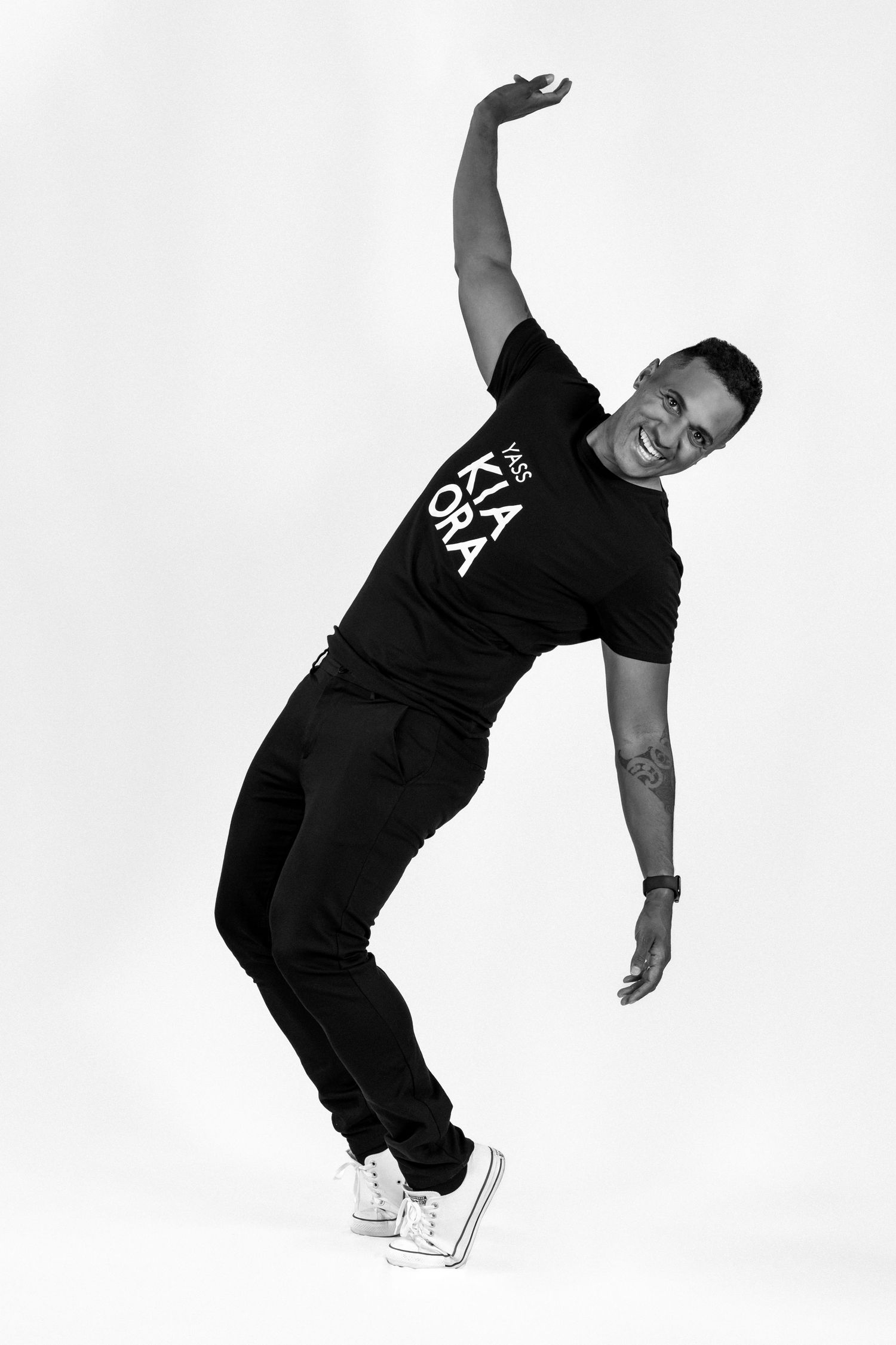 Black and white image of a Maori man. He is having fun posing for the camera. Full length image. Kia Ora text on his t-short. Branding shoot