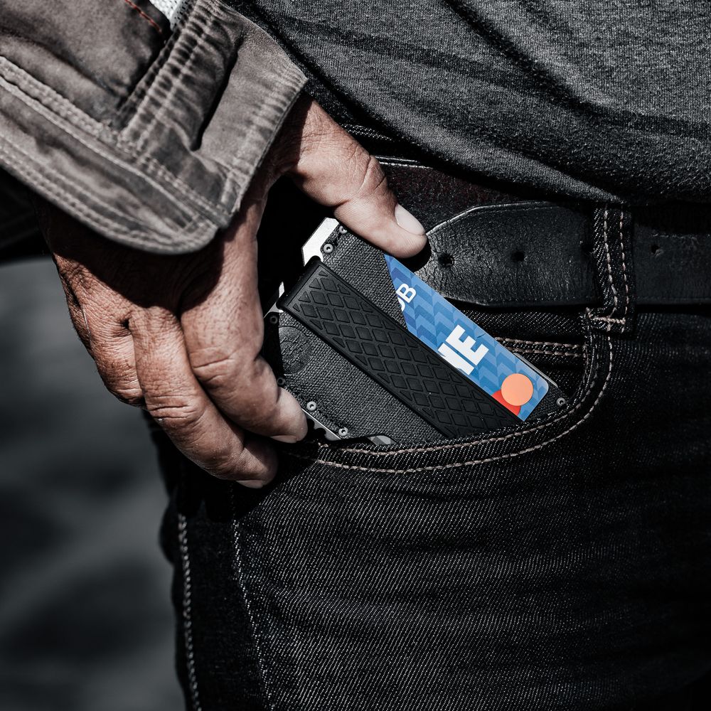 Close-up of a man pulling a slim card wallet with credit cards from black jeans pocket.