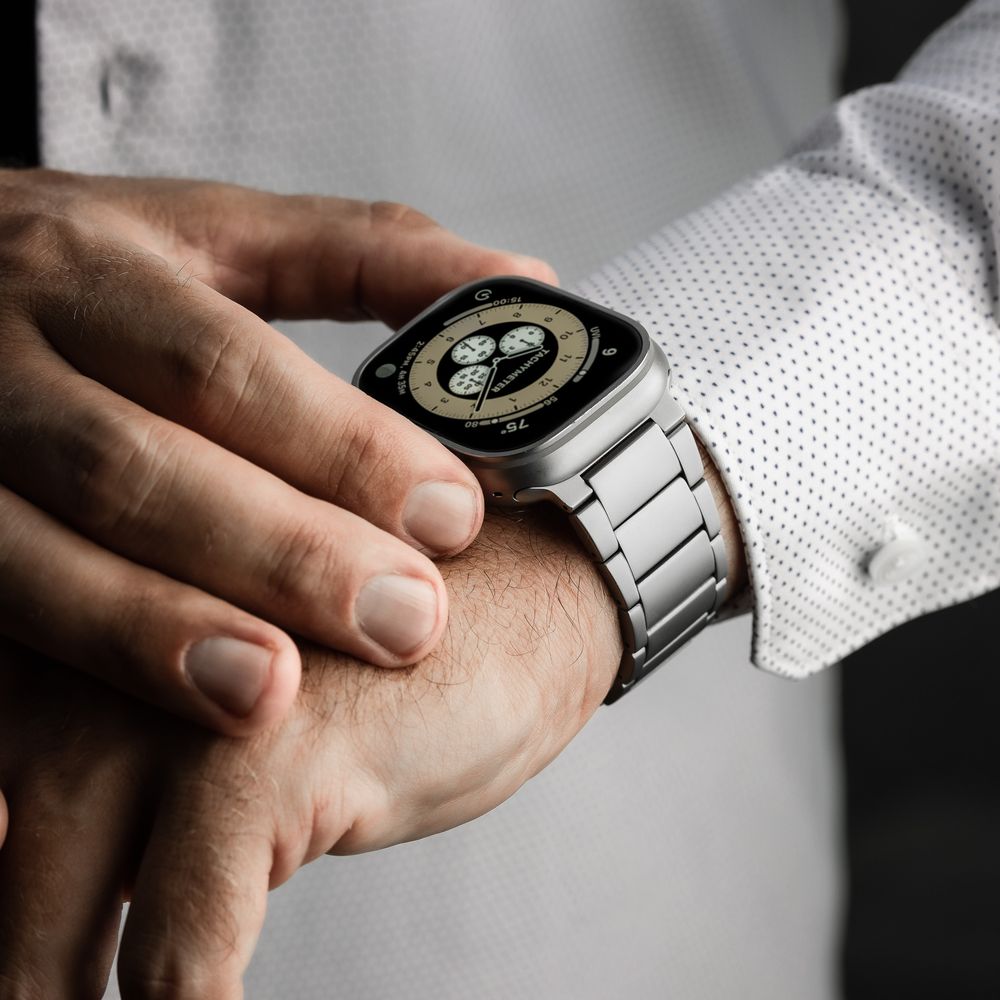 Man wearing a silver Apple Watch Ultra with a metal link band on his wrist, dressed in a white button-up shirt.