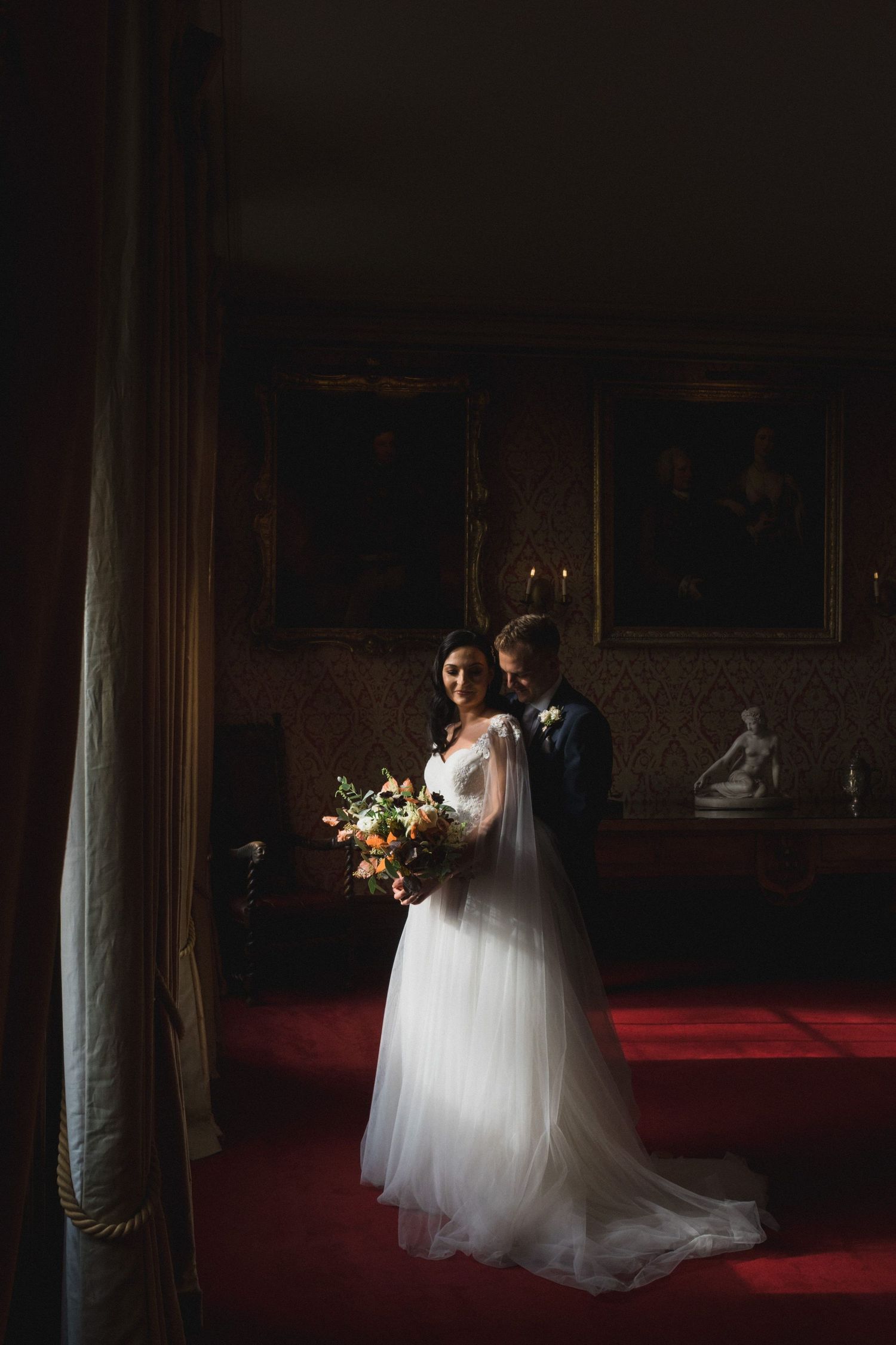 Bride and groom share a romantic moment in an elegant, dimly lit room, bride holding an autumn bouquet.