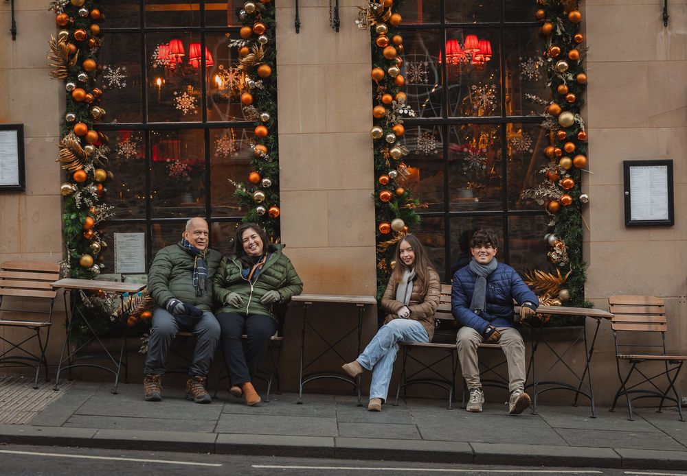 Family of four sitting on benches outside a festively decorated restaurant with orange garlands at Christmas.