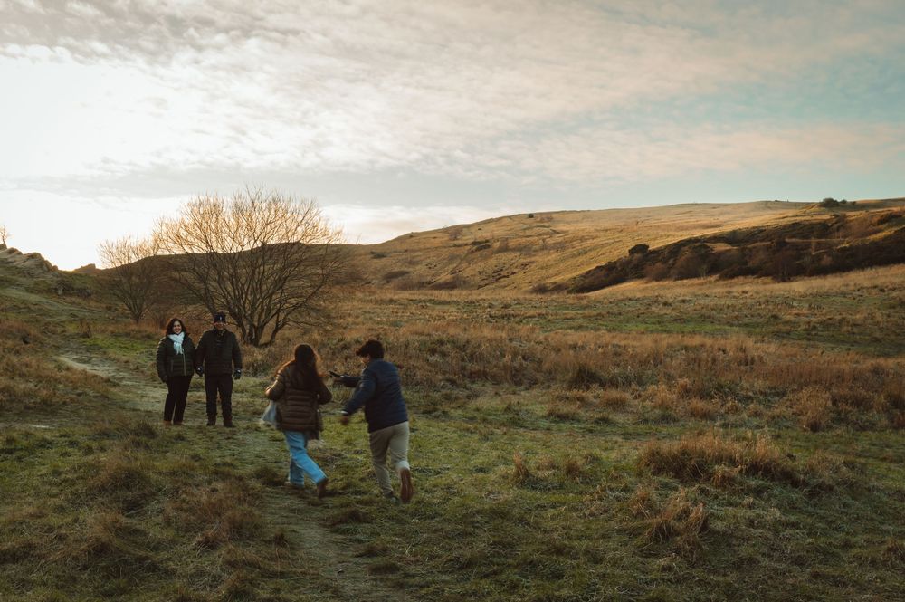 Group of people hiking on a scenic trail through golden grasslands under a cloudy sky at sunset.
