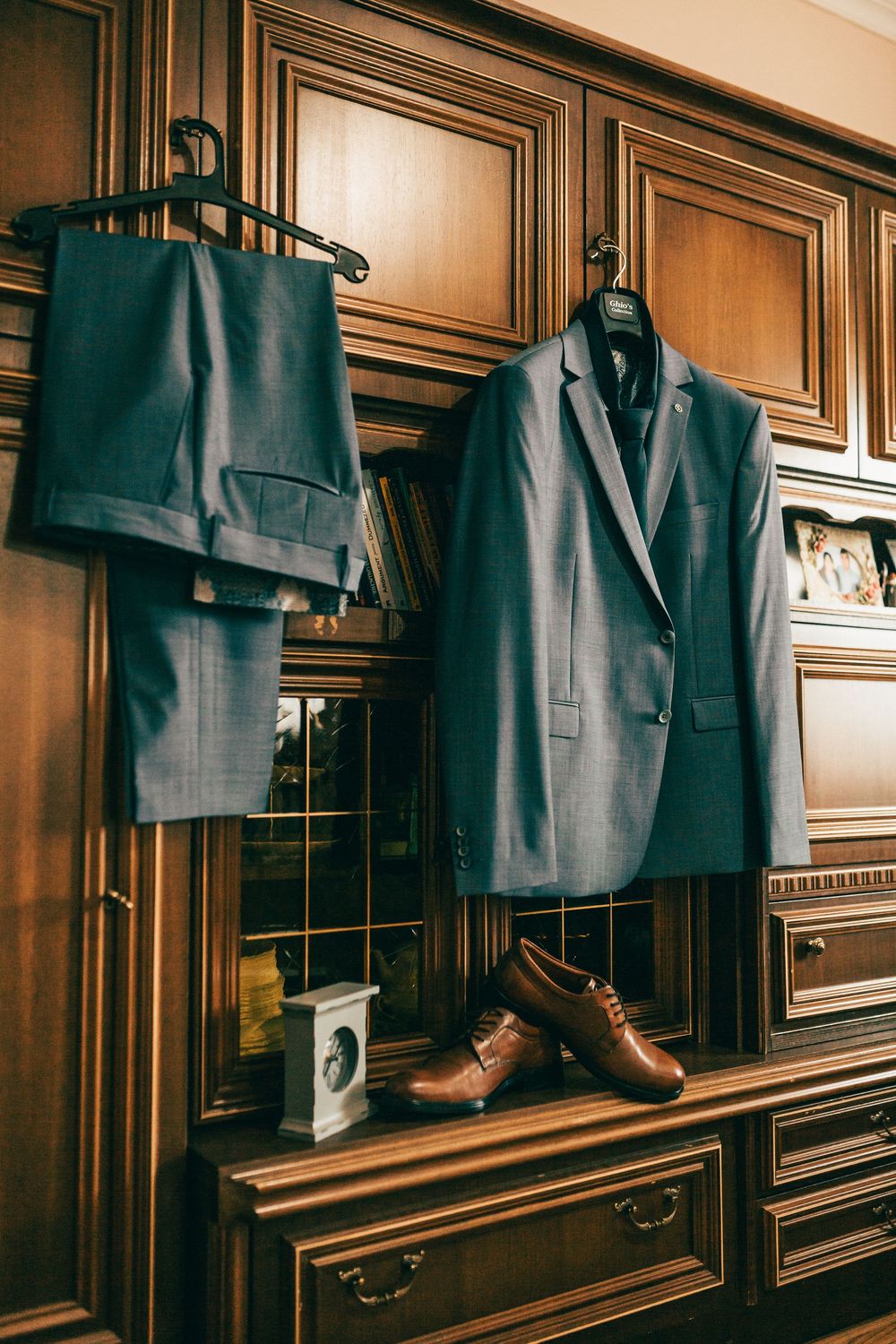 Navy blue suit jacket and trousers hanging on wooden wardrobe with brown leather dress shoes below.