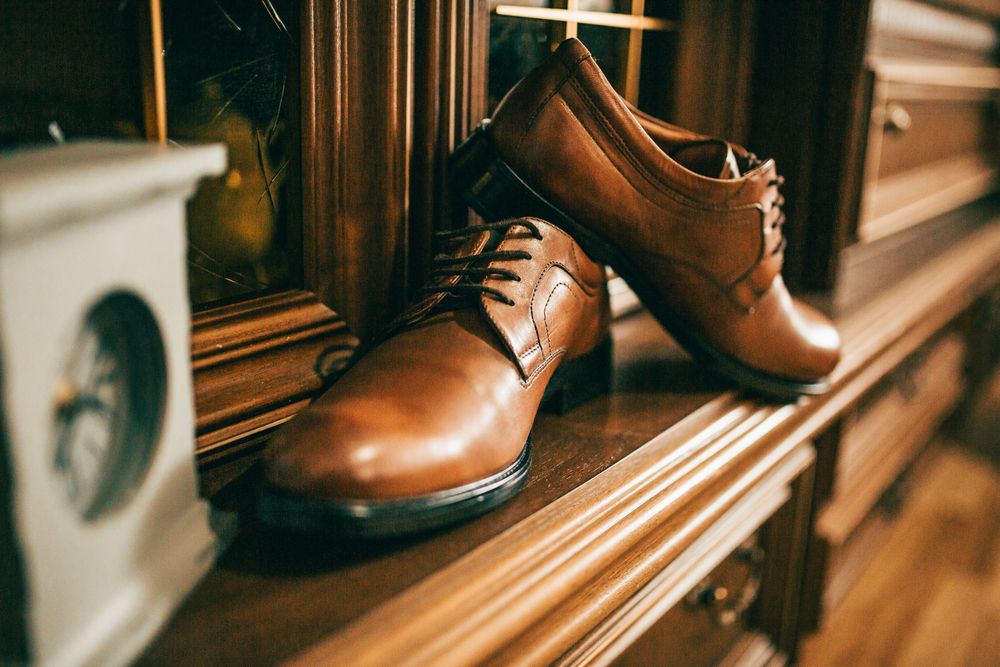 Brown leather oxford dress shoes displayed on a wooden shelf in a classic shoe store.