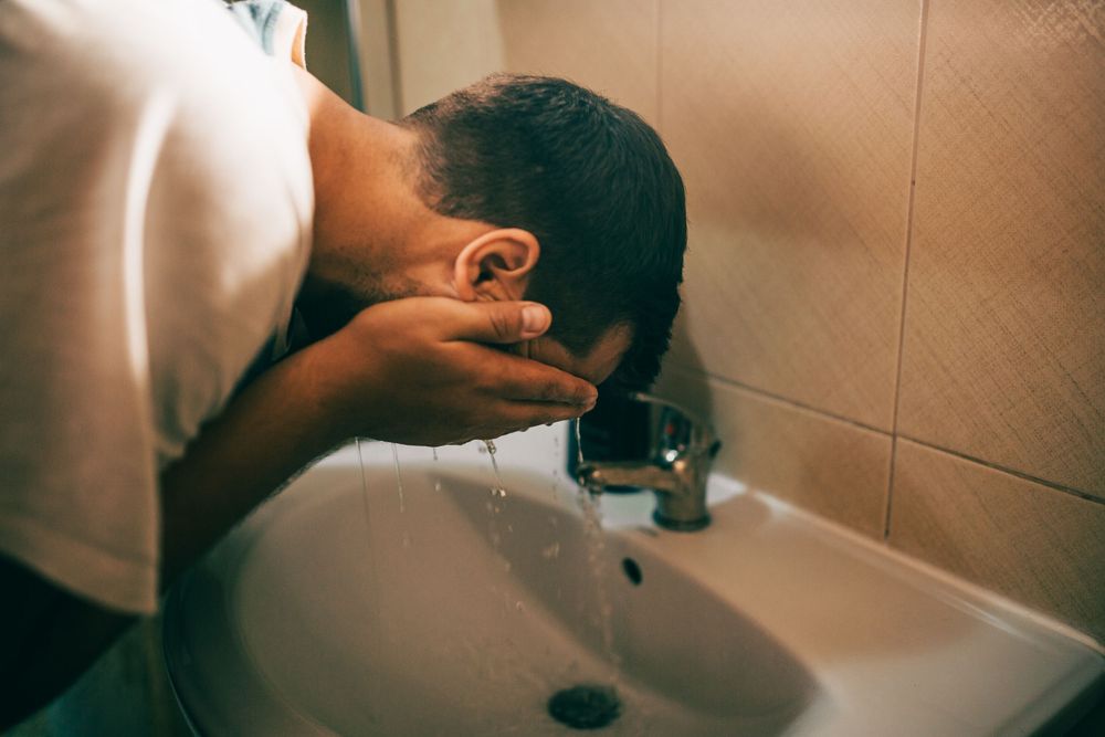 Man washing his face over a bathroom sink with running water.