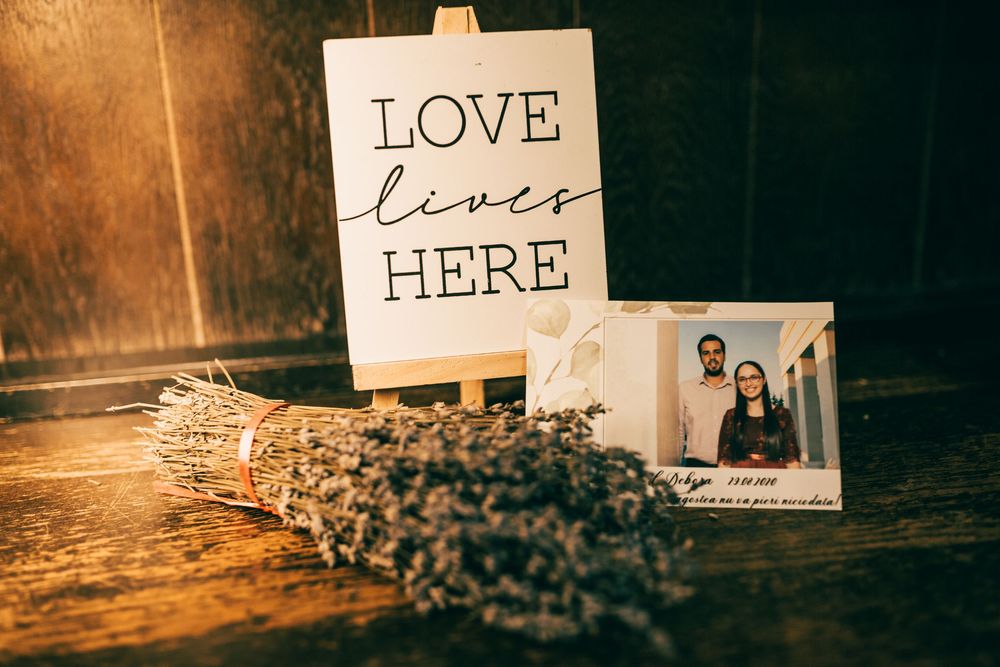 Romantic wedding decor with Love Lives Here sign, dried lavender bouquet, and couple photo on rustic wooden table.