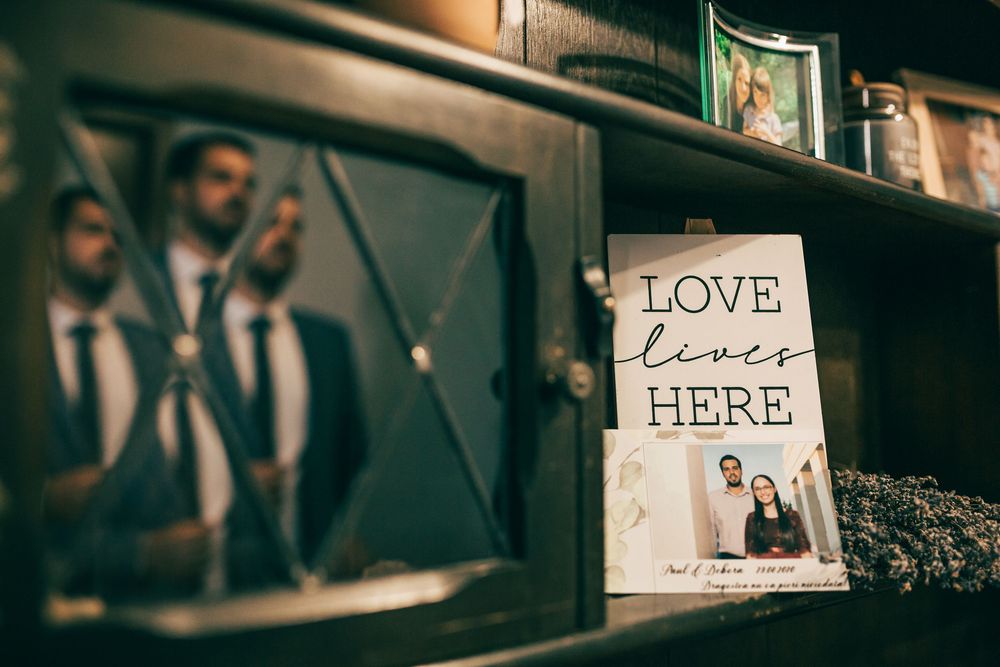 Love Lives Here wedding sign displayed on shelf with groom reflection in cabinet mirror at reception venue.