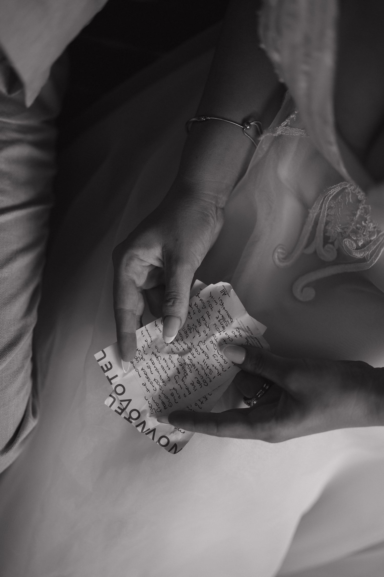 Black and white photo of hands holding a small cross and paper note on flowing fabric.