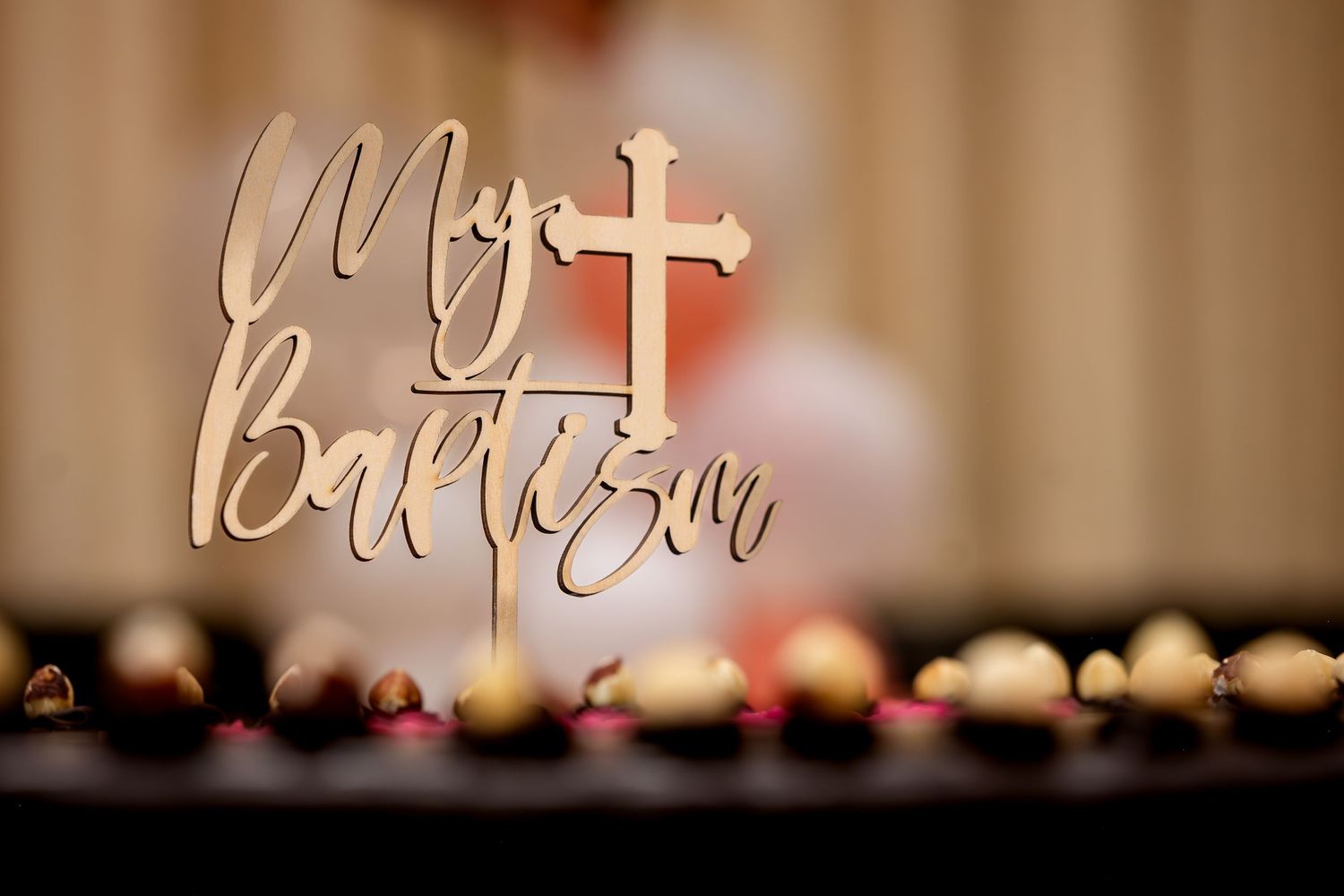 Gold My Baptism cake topper with cross on a table decorated with gold and pink ornaments.