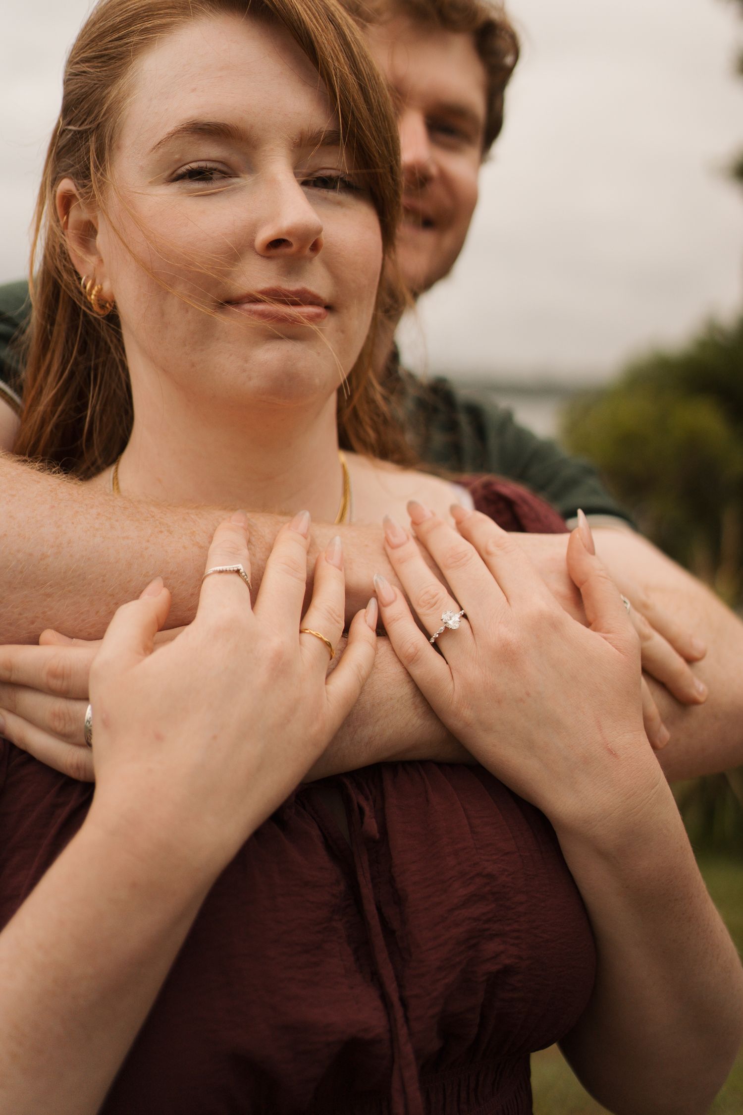 Engaged couple embracing outdoors, woman showing diamond engagement ring and wedding band on her left hand sydney proposal