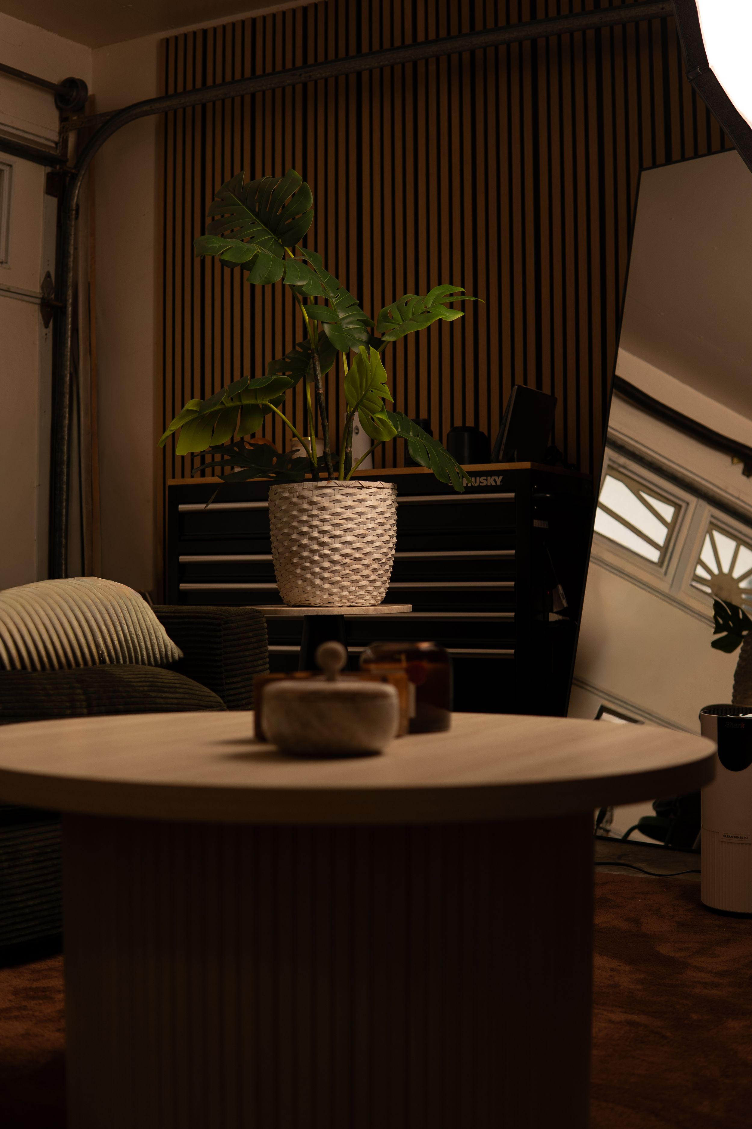 Cozy dimly lit room with a round wooden table, potted tropical plant, and acoustic wall panels in warm tones.