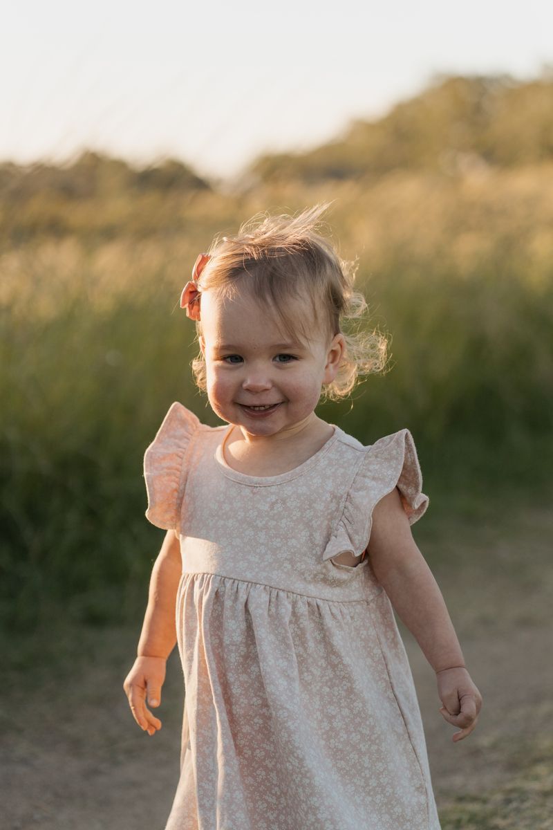 Smiling toddler girl in a floral dress playing outdoors in a sunlit field at golden hour in rouse hill family photoshoot