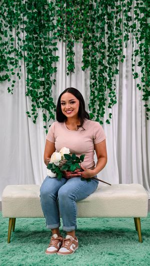 Woman in pink tee and jeans holds white roses on white bench with hanging green ivy backdrop.