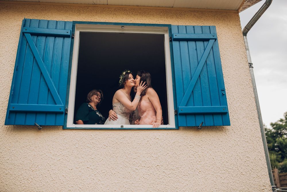 Bride and groom share a romantic kiss through an open blue shuttered window.