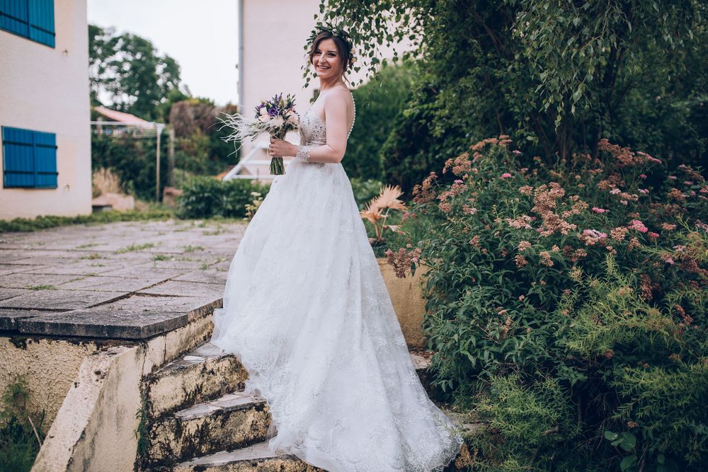 Elegant bride in white ball gown holds bouquet while posing in a garden.