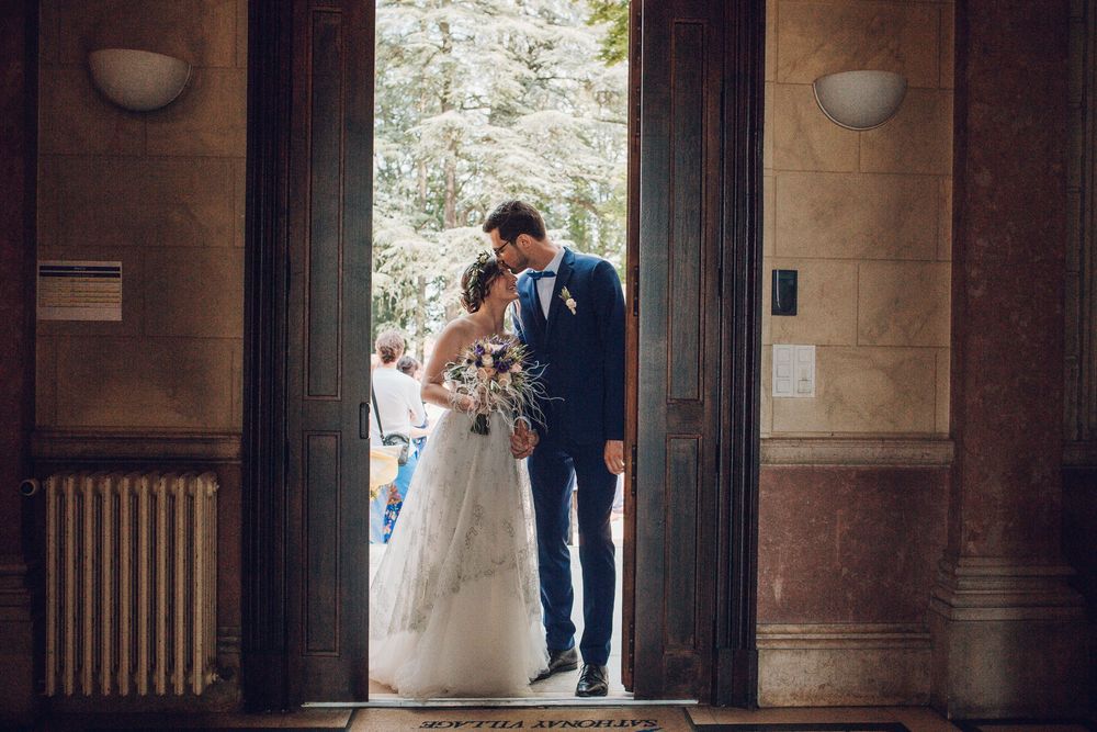 Bride and groom share tender moment in doorway of elegant venue, bride holding bouquet in white gown.