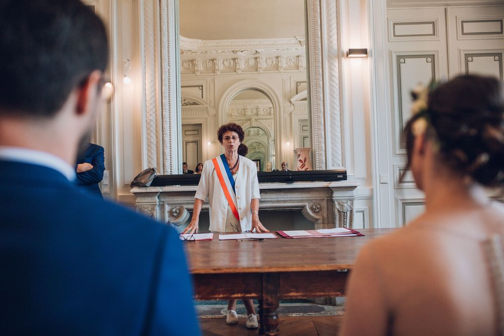Official in tricolor sash presides over civil wedding ceremony at ornate French town hall.