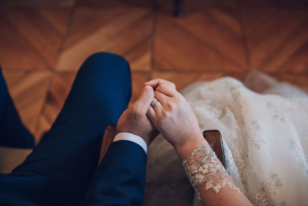Close-up of bride and groom holding hands, showcasing wedding ring and lace bridal gown detail.